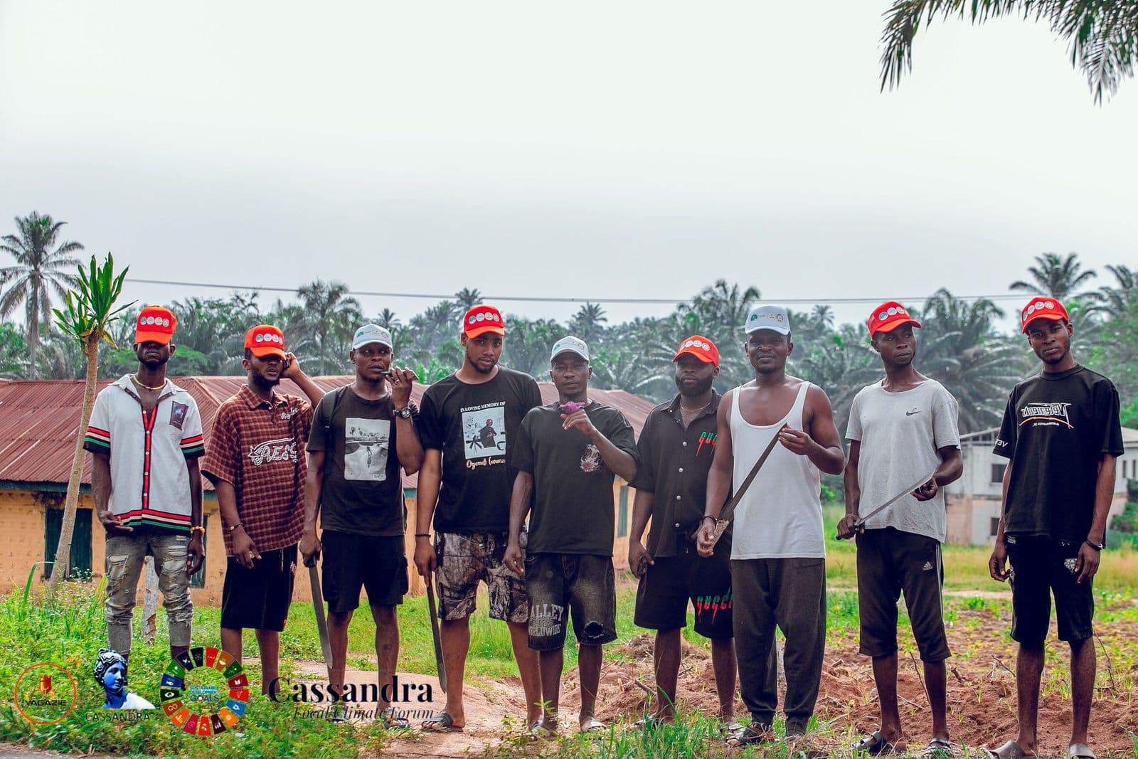 Community volunteers in orange caps line up in front of palm trees near Ugiri