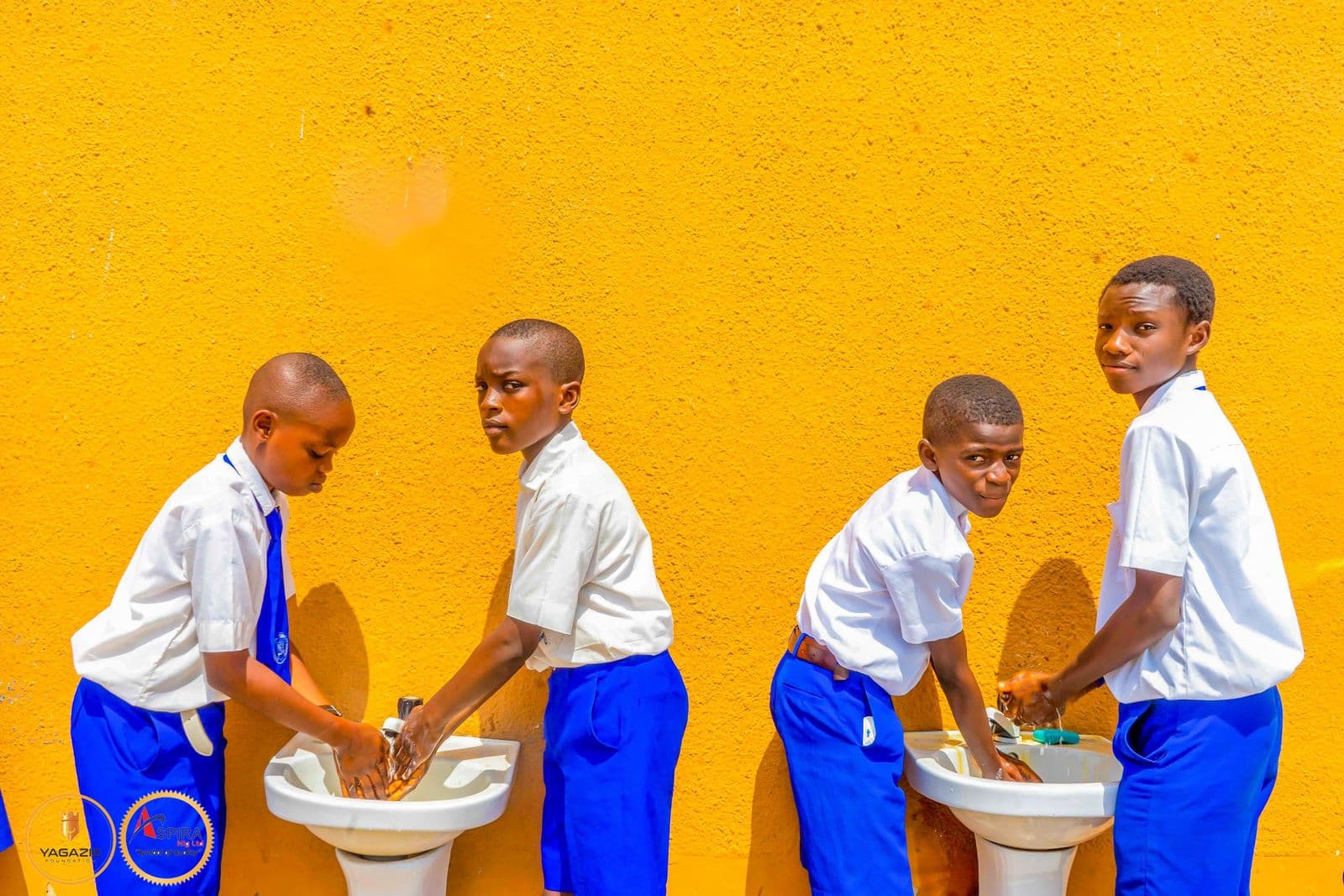 Four boys wash their hands side by side at the hand-washing stations